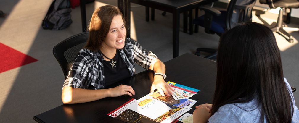 A straight-haired woman smiles warmly towards a client sitting on the other side of a table